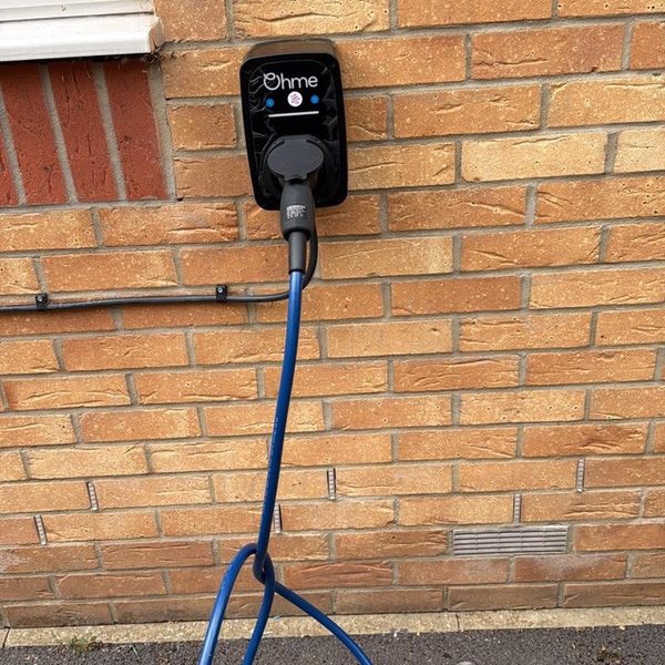 Ohme EV charger with a blue charging cable on a brick wall